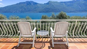 Deux chaises blanches et une petite table ronde sur une terrasse offrant une vue sur un lac et des montagnes.