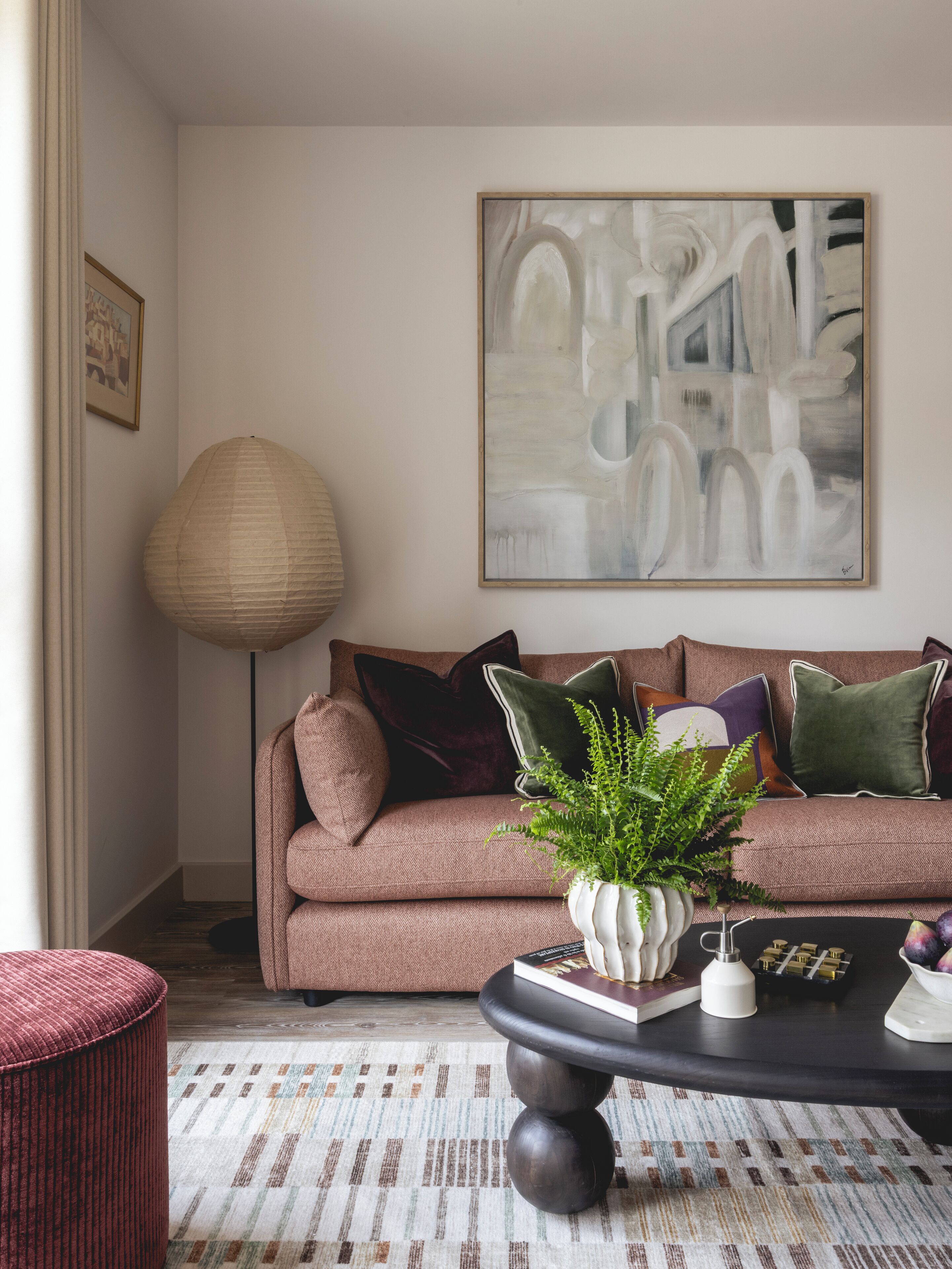 A living room with a brown sofa, a large abstract painting, a floor lamp, and a coffee table with books and decorative items.