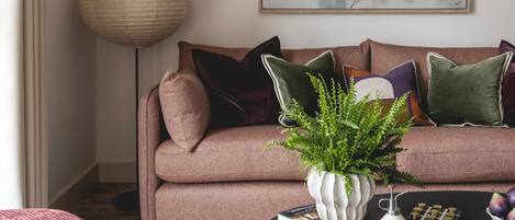 A living room with a brown sofa, a large abstract painting, a floor lamp, and a coffee table with books and decorative items.