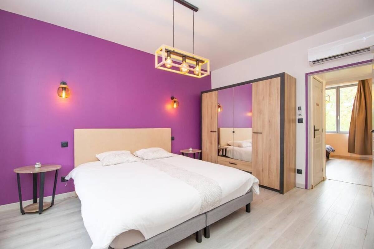 A modern bedroom with a large bed, purple walls, and a wooden wardrobe.