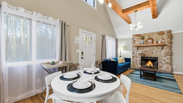 Un coin repas avec une table ronde dressée pour quatre personnes, une cheminée en pierre et un canapé bleu en arrière-plan.