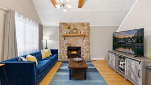 Un salon avec une chemin ée en pierre, un canapé bleu, une table basse en bois et un téléviseur posé sur un meuble en bois.