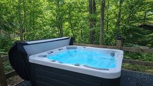 Un bain à remous avec une terrasse en bois et une vue sur une forêt.