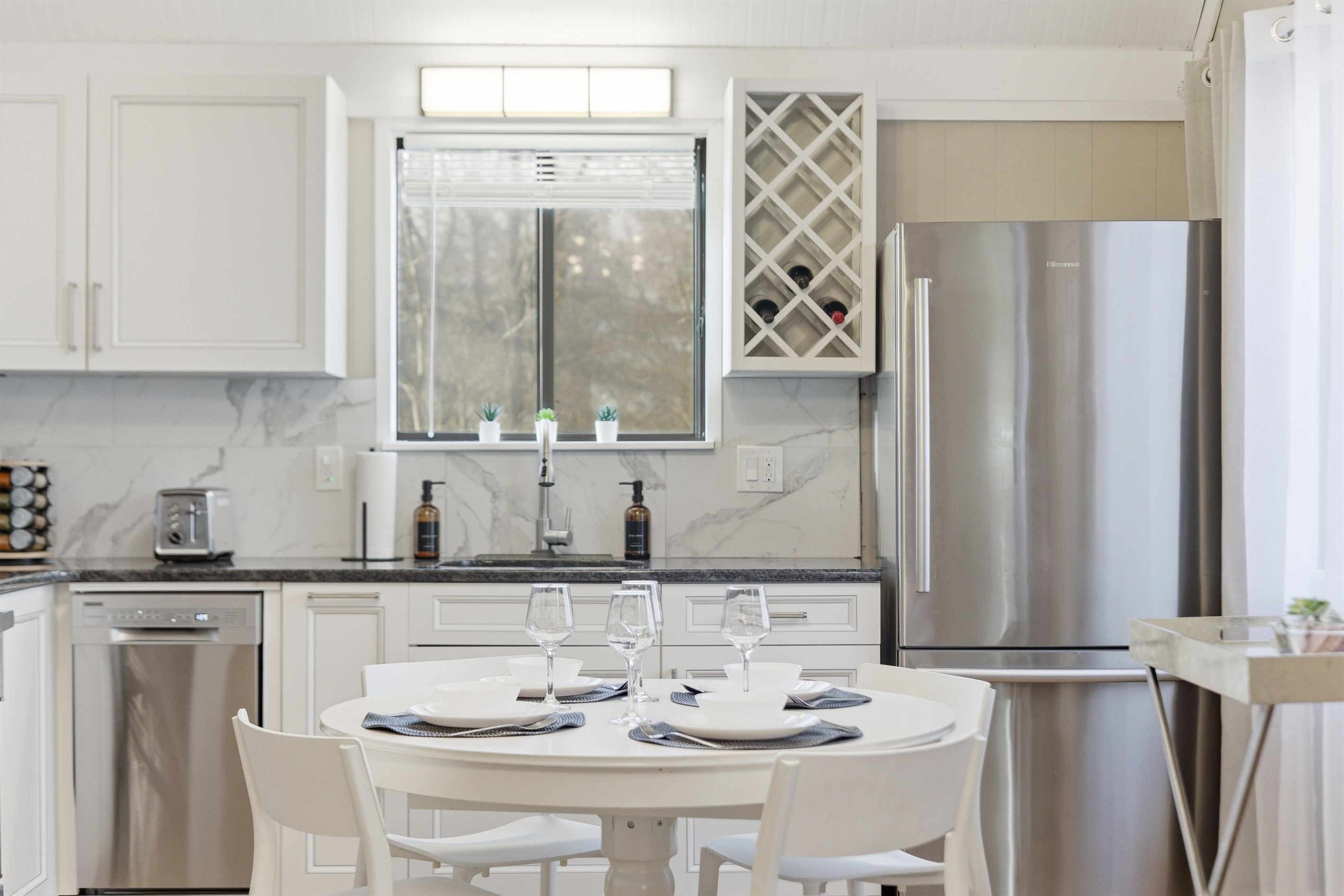 Une cuisine moderne avec des meubles blancs, un réfrigérateur en acier inoxydable et un coin repas comprenant une table ronde et des chaises.