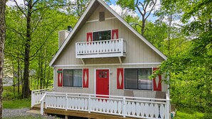 Une cabane à deux étages avec un balcon, entourée d’arbres.