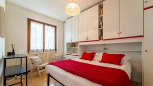 Un dormitorio con cama, escritorio, silla, estantería y ventana.
