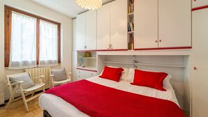 Un dormitorio con cama, una silla, un radiador, una ventana y una estantería.