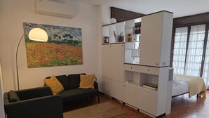 Ein Zimmer mit einer Couch, einem Bett, einem weißen Schrank, einem Gemälde und einem Fenster.