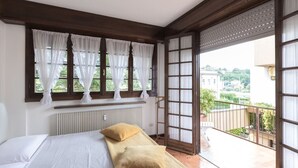 Ein Schlafzimmer mit einem Bett, weißen Vorhängen, einem Heizkörper und Blick auf einen Balkon mit Geländer.