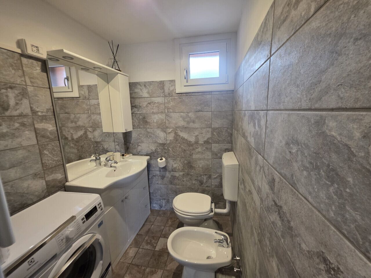 A compact bathroom with a sink, toilet, and washing machine.