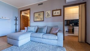 Ein modernes Wohnzimmer mit einem grauen Ecksofa, einem kleinen Teppich und einer durchgehenden Tür erkennbaren Küche.