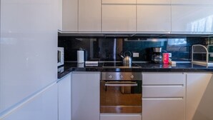 Eine moderne Küche mit weißen Schränken, einer schwarzen Arbeitsplatte, einem Wasserkocher, einer Kaffeemaschine und einer Mikrowelle.