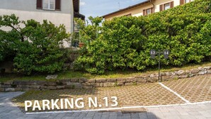 Ein gepflasterter Parkbereich mit einer Steinmauer und Bepflanzung, mit der Beschriftung "PARKING N.13".
