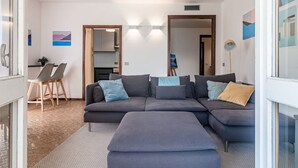 A modern living room with a sectional sofa, a small dining area, and a kitchen visible through an open door. - Ca` Maria Acero Apartment (Bellagio)