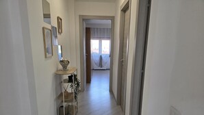 Un couloir doté d’un plancher en bois, une petite table avec un panier, et une porte donnant sur une pièce avec une fenêtre.