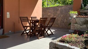 Une terrasse extérieure avec un mur en pierre, une table avec des chaises et un petit espace aménagé en jardin.