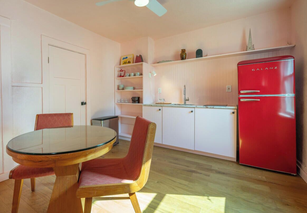 A compact kitchen with a round glass table, two chairs, a red refrigerator, and white cabinetry.