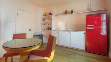 A compact kitchen with a round glass table, two chairs, a red refrigerator, and white cabinetry.