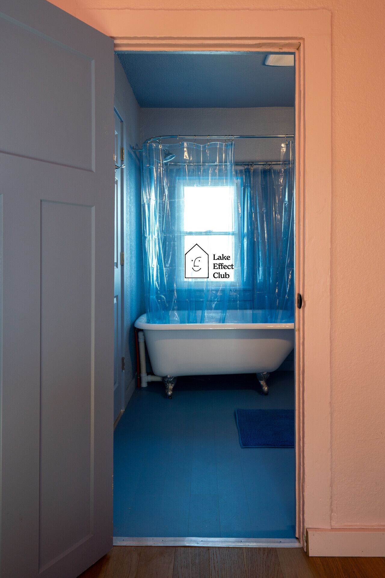 A bathroom with a bathtub, a window with a curtain, and a sign indicating 'Lake Effect Club'.