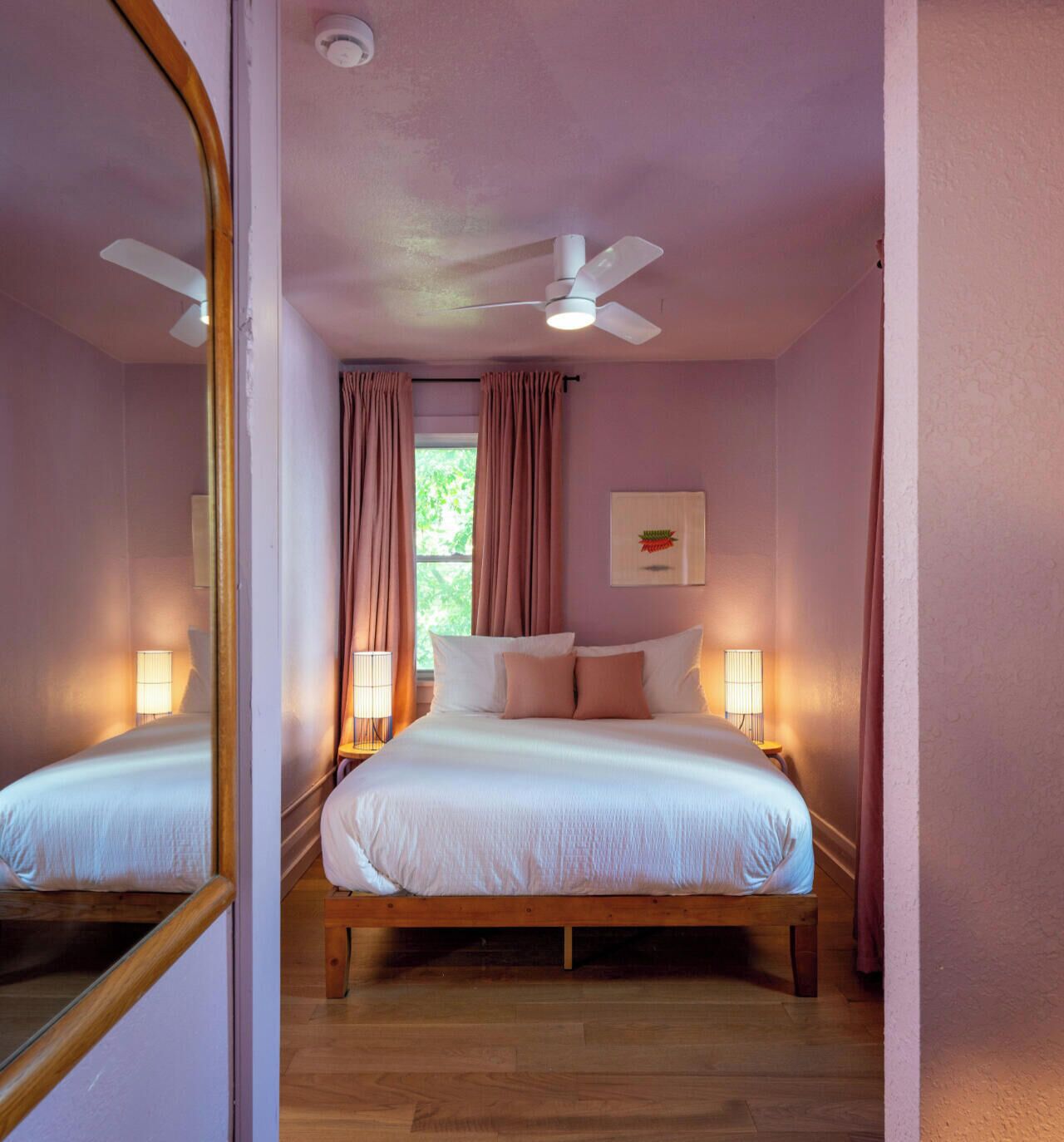 A bedroom with a bed, a ceiling fan, a window with curtains, and a wall-mounted light fixture.