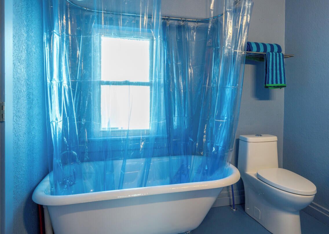 Un bagno con una vasca, un water e una finestra con tenda blu.