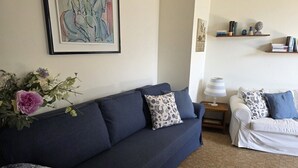 Ein Wohnzimmer mit einem dunkelblauen Sofa, einem weißen Sofa, einem gerahmten abstrakten Gemälde und einem kleinen Bücherregal.