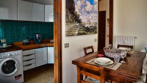 Eine kompakte Küche mit modernen Geräten, ein Essbereich mit Tisch für zwei Personen und ein großes Landschaftsbild an der Wand.