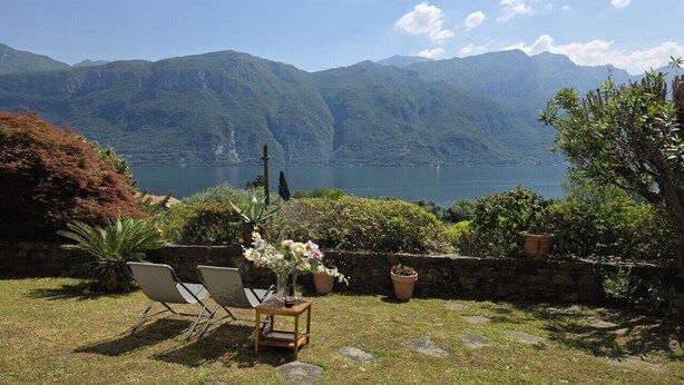Eine Terrasse mit Stühlen und einem Tisch, mit Blick auf einen See und Berge.