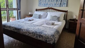 Ein ordentlich bezogenes Bett mit einer blumigen Tagesdecke, einem hölzernen Kopfteil und einem Nachttisch mit Lampe.