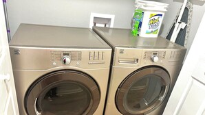 Twee Kenmore wasmachines met voorlader in een wasserette met een witte deur en een plank bovenop met een wasmiddelbox en een mes.