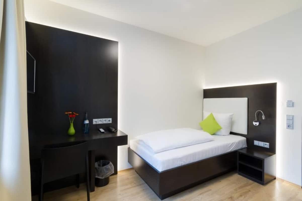 Een moderne hotelkamer met een bed, nachtkastje en een bureau met stoel.