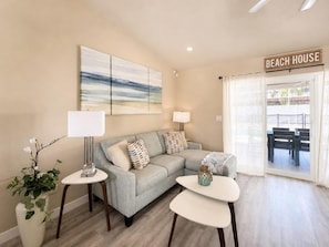 A living room with a sofa, two side tables, a lamp, a vase with flowers, and a beach-themed sign. - Heated Pool & Jacuzzi Pet Friendly- 7 min to Beach No Extra Fees (Palm Coast)