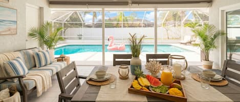 A dining area with a pool view, a sofa, and a fruit tray.