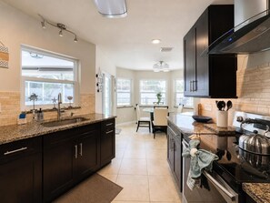 A modern kitchen with dark cabinetry, granite countertops, a central island, and a stove. - Heated Pool & Jacuzzi Pet Friendly- 7 min to Beach No Extra Fees (Palm Coast)