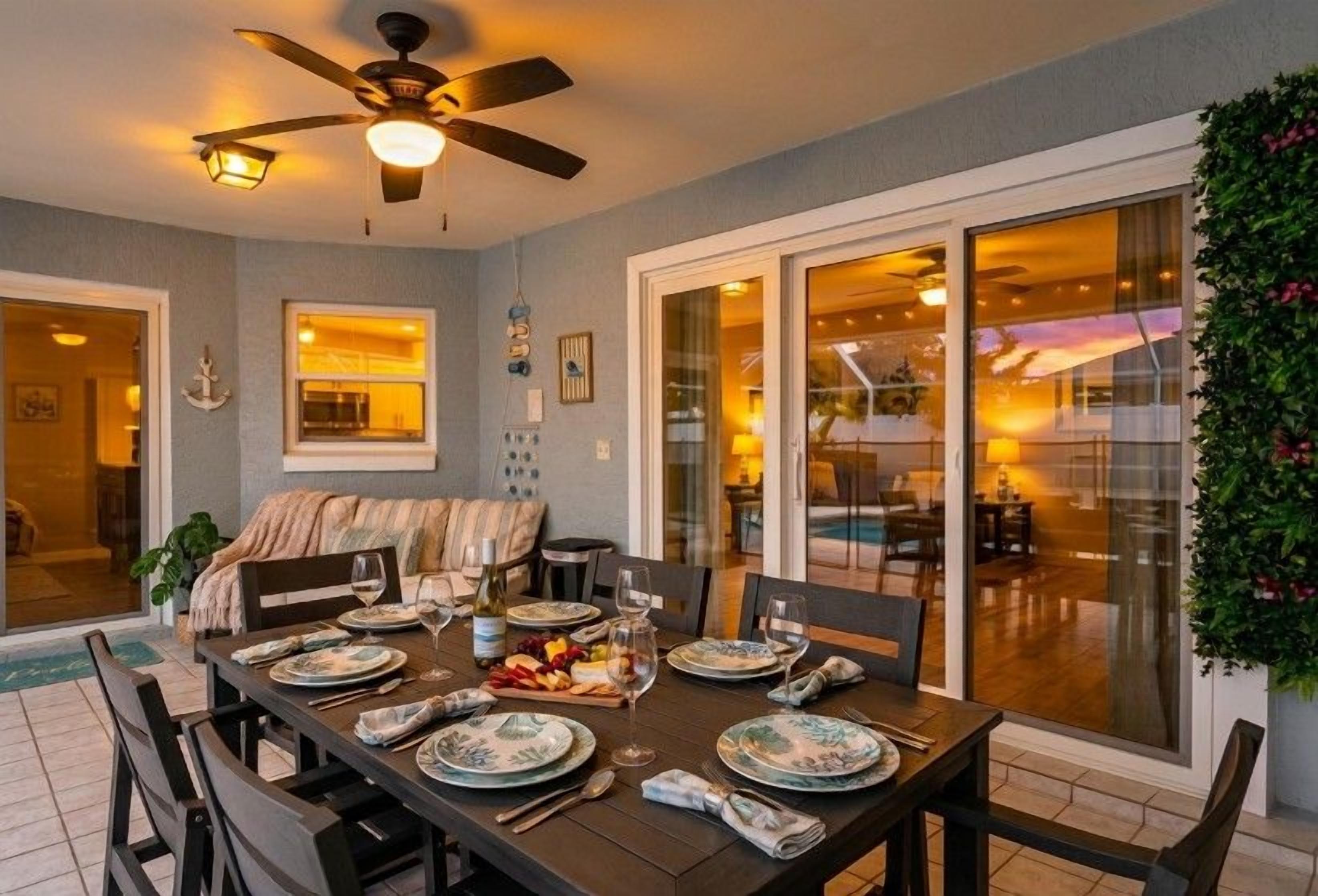 Comedor con mesa lista para cuatro, ventilador de techo y vista a un espacio exterior a través de puertas de vidrio.