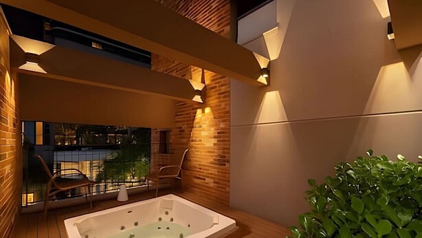 Un espace moderne aménagé à l’extérieur avec un bain à remous, une terrasse en bois et un coin salon avec des chaises, offrant une vue sur le paysage urbain.