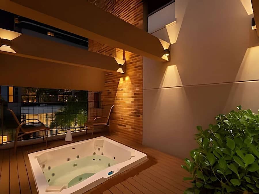 Uma área externa moderna com hidromassagem, deck de madeira, espaço de estar com cadeiras e vista para a paisagem urbana.