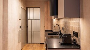 A narrow kitchen with a wooden floor, a black range hood, a sink, and a coffee machine. - Dobo Madrid MA24 (Madrid)