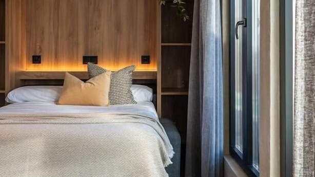 A modern bedroom with a wooden headboard, a ceiling fan, a large window with curtains, and a bedside table. - Dobo Madrid MA24 (Madrid)