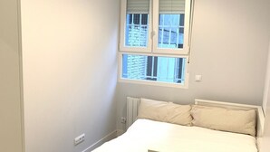 A small bedroom with a bed, a radiator, a window with blinds, and a door. - Urban suites Aluche (Aluche)