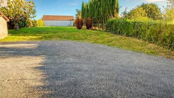 Une allée de gravier mène à un bâtiment doté d’un toit en pente, qui est entouré de verdure et d’arbres.