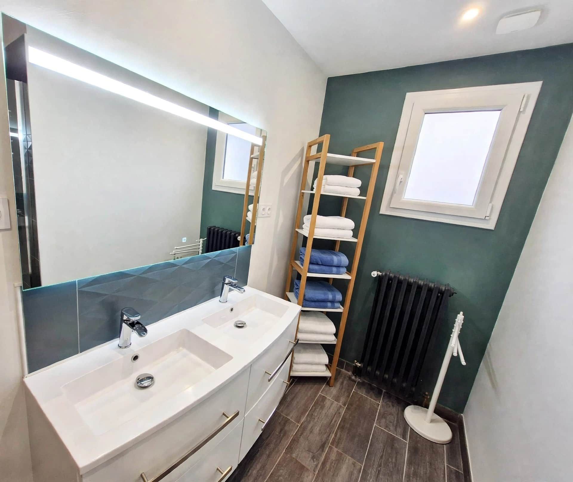 A bathroom with a large mirror, two sinks, a towel rack, and a radiator.