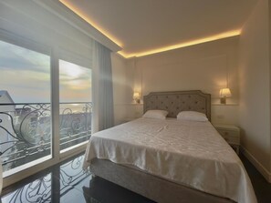 A hotel room with a large bed, two bedside lamps, a nightstand, and a balcony with a metal railing. - Golden Crown  (Sveti Stefan)