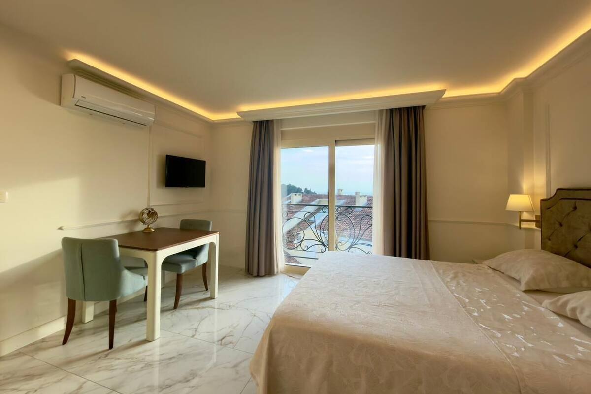 A hotel room with a bed, a desk, a chair, a TV, and a balcony with a view.