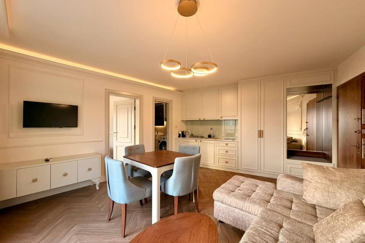 A modern living room with a dining area, a sofa, and a TV mounted on the wall.
