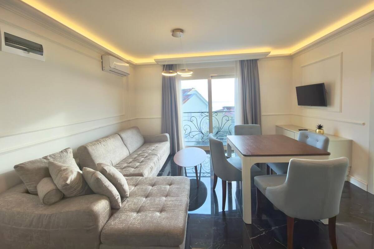 A modern living room with a sofa, dining table, chairs, and a TV mounted on the wall.