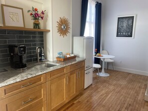 A modern kitchen with wooden cabinets, a coffee maker, a sink, and a small dining area with a table and chairs.