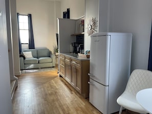 A compact kitchen with wooden cabinets, a white refrigerator, and a dining area with a white chair.