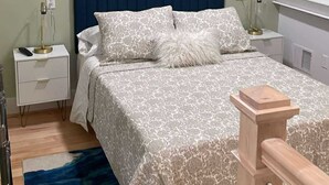 A bedroom with a bed, nightstands, a painting, and a blue rug.