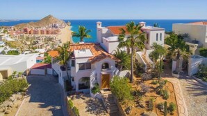 A coastal residential area with white buildings, palm trees, and a view of the ocean. - Pedregal Penthouse with Breathtaking Views (Cabo San Lucas)